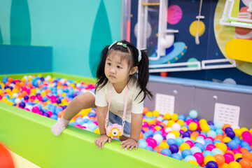Fototapeta premium Little Asian girl playing with interactive ball wall at indoor playground,An adorable young Asian girl is focused on playing with an interactive ball physics game and a colorful ball pit at a modern.