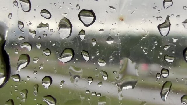 Rain drops on glass with traffic passing by 
