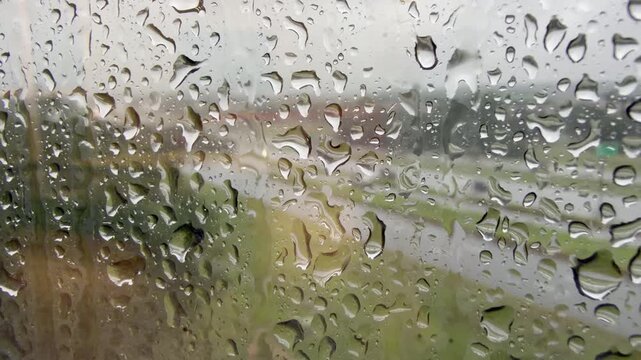 Rain drops on glass with traffic passing by 