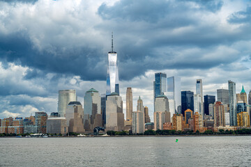 Obraz premium Financial District skyline with One World Trade Center. Daytime view of Manhattan skyscrapers from the water, Hudson River foreground, overcast sky.