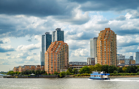 Modern residential buildings on waterfront with ferry boat. Contemporary brick apartment buildings at waterfront, blue ferry boat on river, cloudy sky, urban landscape.