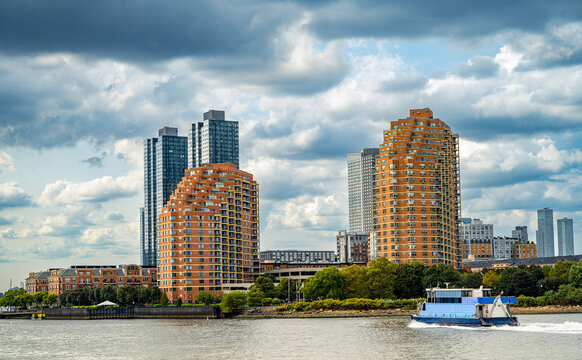 Waterfront apartment complex with passing blue ferry boat. Curved modern residential architecture on riverbank, passenger ferry on water, cloudy sky, urban housing.