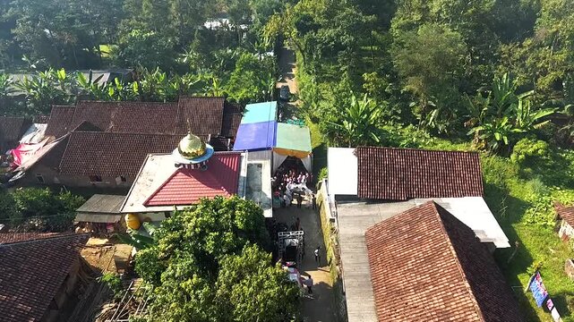 Aerial view of a traditional wedding procession in a narrow Indonesian village alley.