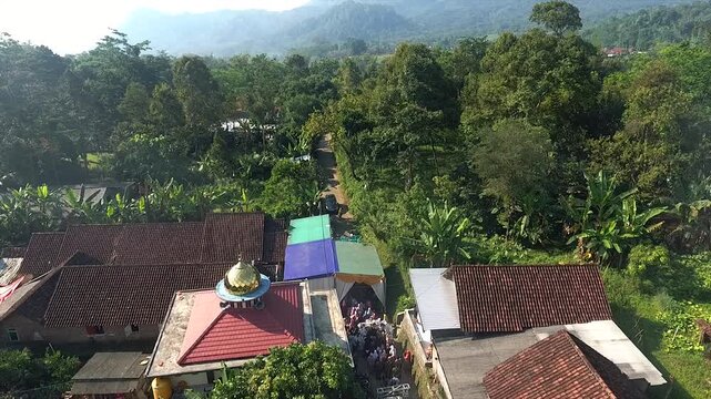 Aerial view of a traditional wedding procession in a narrow Indonesian village alley.