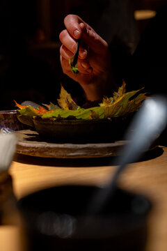 Gros plan sur une main utilisant une pince de pr&eacute;cision pour composer un plat gastronomique sur un lit de feuilles d'automne, dans une ambiance tamis&eacute;e et minimaliste au style raffin&eacute;.