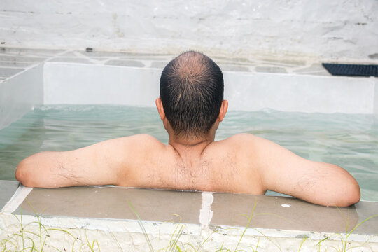 back view of bare man chilling in a swimming pool without device during vacation. 