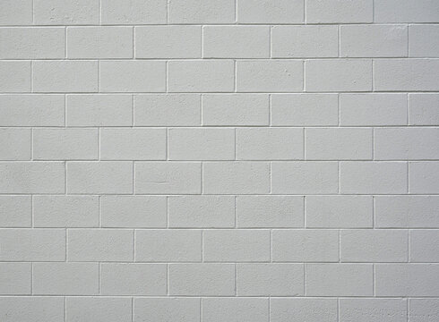 Close up of painted white cinder block wall with rough coarse concrete blocks, smooth mortar grooves, long gouge in one block, and soft natural lighting