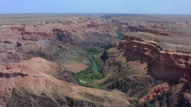 Aerial wide panorama of Charyn Canyon with winding river cutting through dramatic layered cliffs and vast arid plateau, cinematic drone flight revealing scale, texture and remote wilderness landscape