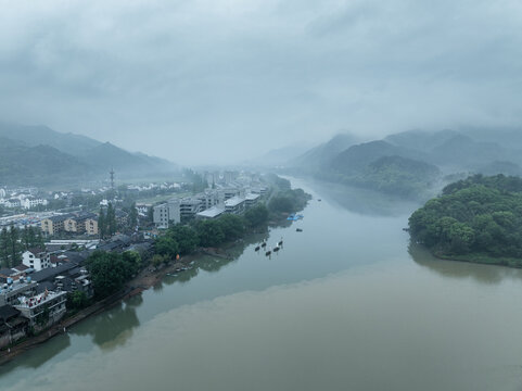 A misty riverside view of a traditional Jiangnan water town with ancient buildings and distant mountains