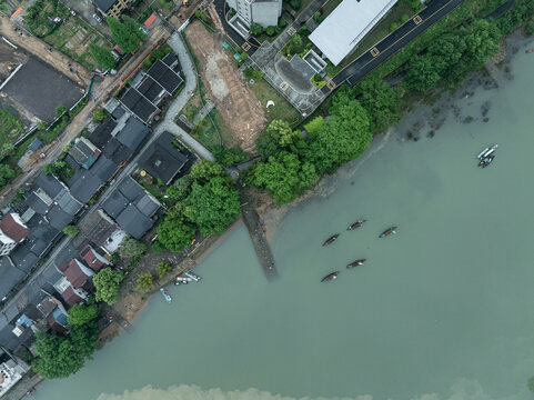 Aerial view of riverside village with fishing boats moored and green trees surrounding traditional houses