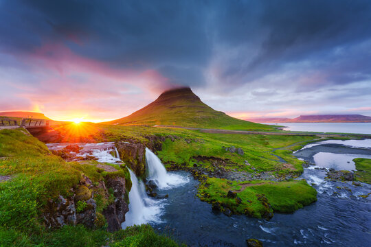 Kirkjufell mountain waterfall with dramatic cloudy sky and golden sunset in Iceland