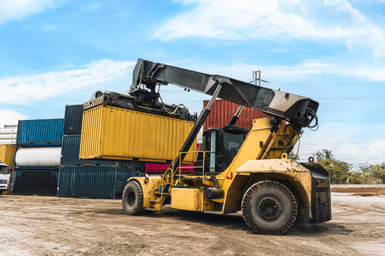 Loaded container handler forklift moving cargo container in crowded shipping yard at port terminal