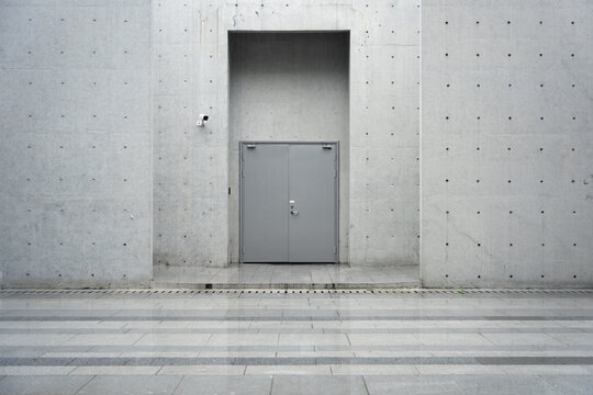 Gray concrete wall with embedded metallic double door entrance in modern architectural setting