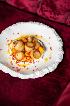 A gourmet dessert plate on a plush velvet surface, featuring pan-seared dumplings or cheese pancakes topped with fruit pieces and bright red crumbles on a creamy white base.