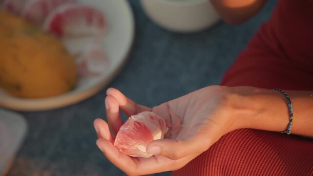 Peeling grapefruit on beach picnic sunset, closeup of hands gently separating segment over bowl and plate, soft golden light, warm tones, bracelet on wrist, relaxed couple ceremony vibe, tea set