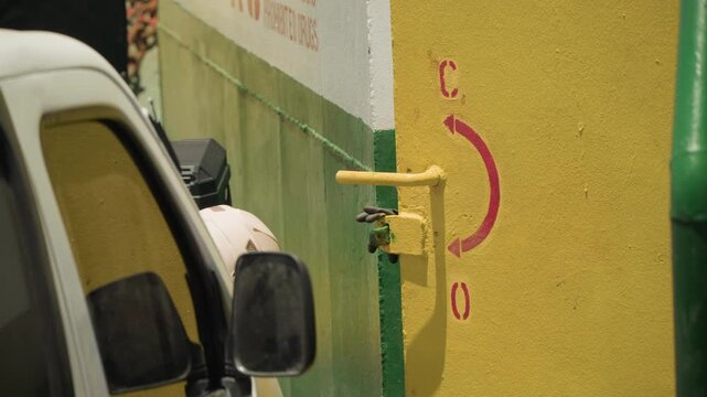 Yellow wall beside parked van, green pipe with yellow valve, stucco texture and faded graffiti, close framing of side mirror and vehicle panel, daytime gritty cinematic mood perfect for transport