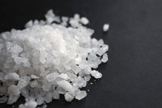 Close-up of a pile of coarse white sea salt crystals on a dark background