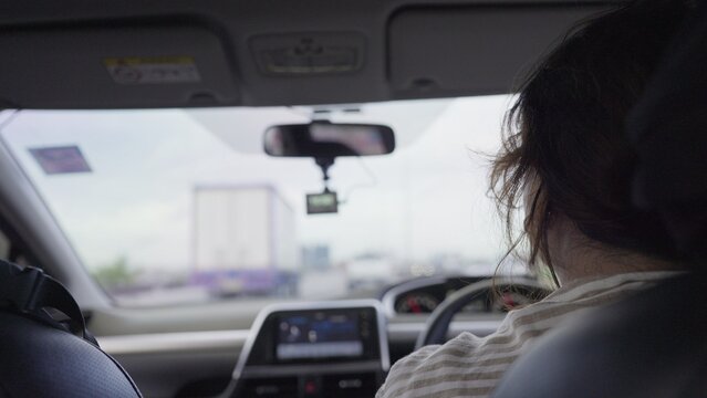 A woman driver navigates through highway traffic during her daily commute, viewed from the back seat of the car with a dashcam recording the journey ahead.