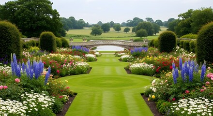 Obraz premium Grand symmetrical English estate garden with twin stripes of perfectly mown lawn flanked by mirror‑image borders of blue spires soft roses and white daisies leading toward terraces bridge and distant 