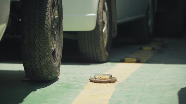 Car wheel beside rusted anchor ring, tight parking composition showing tire tread and rim in foreground with painted bay stripe emphasis on clearance, safety risk, inspection and urban garage