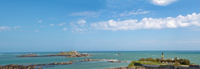 Wide panoramic seascape showing a ribbon of cloud crossing the picture set against a blue sky. A lighthouse stands to the right of frame in this rugged coastal scene.  © Steven