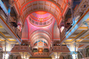 A symmetrical wide-angle interior shot of a grand hall featuring Thai-European neo-classical architecture. The image highlights a majestic vaulted ceiling with intricate patterns, a central dome © Hathaichanok