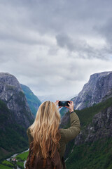Naklejka premium Woman, adventure or mountain with phone for picture of landscape, outdoor memory or photography. Back view, female person or tourist with smartphone for travel or capture moment of natural scenery