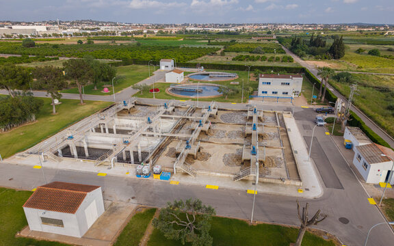 Top-down view of a biological WWTP featuring activated sludge aeration tanks with surface aerators, rectangular sequencing basins, and circular secondary clarifiers surrounded by green agricultural la
