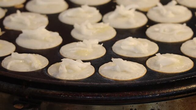Close Up of Traditional Thai Coconut Pancakes (Khanom Khrok) Topped with Shredded Coconut Cooking on a Special Cast Iron Griddle