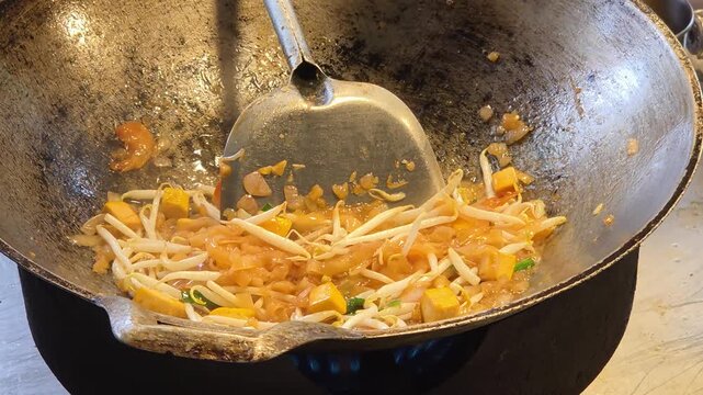 Chef Stir-Frying Pad Thai Noodles with Tofu and Bean Sprouts in a Large Wok over an Open Flame