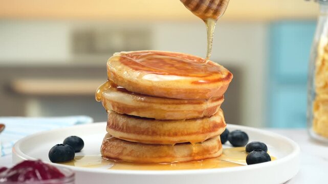 Fluffy pancakes stack with honey drizzle and blueberries on white plate, copy space