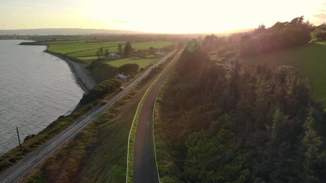 Drone glides smoothly over serene Irish coastal road at sunset, offering breathtaking views and a sense of freedom and exploration.
