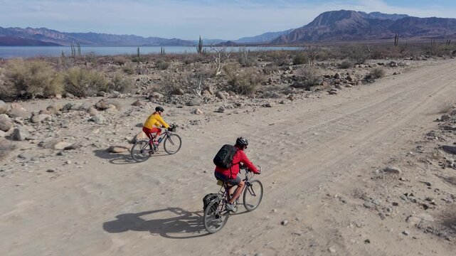 Mature man and woman bike along a trail in La Gringa near Bahia De Los Angeles by the Sea of Cortez in Baja California Mexico under a clear sky.