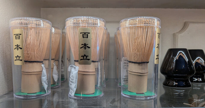 Stockholm, May 30, 2022: Close-up of traditional bamboo matcha tea whisks in clear containers with Japanese labels, neatly arranged on a shelf beside ceramic items in a calm indoor setting.