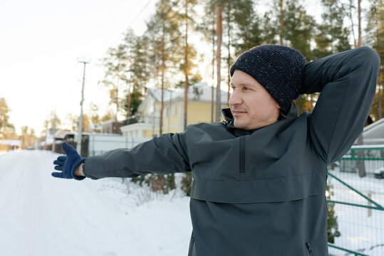 A guy in his forties performs neck and shoulder exercises outdoors. He warms up on a cold morning, focusing on upper spine and muscle health.