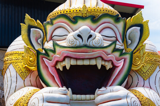 A large-scale outdoor sculpture of Hanuman, the Hindu monkey deity, depicted in the iconic scene of yawning to create a protective pavilion. This Thai architectural art features intricate golden 