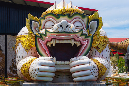 A large-scale outdoor sculpture of Hanuman, the Hindu monkey deity, depicted in the iconic scene of yawning to create a protective pavilion. This Thai architectural art features intricate golden 