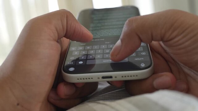 Close-up macro shot of anonymous male hands typing and chatting on a smartphone, fingers tapping a touchscreen keyboard while sending text messages in a modern digital environment. Unrecognizable pers