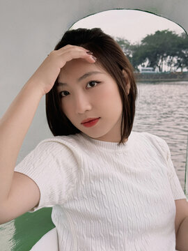 Young woman sits by water in a boat during daytime while shielding her eyes from sunlight
