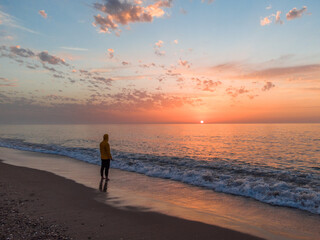 Lonely man relaxing on the beautiful beach at sunset. Sun reflected on beach, Lonely man stands on the beach looks towards the sun light. A man meets the sunset on beach, silhouette of person walking. © Mediterranean sea