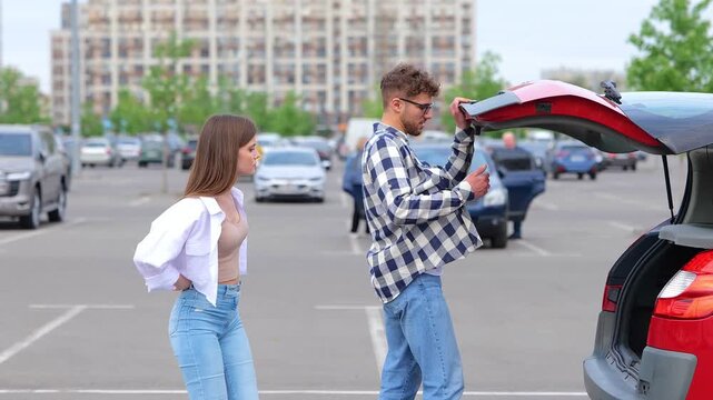 Young couple taking out travel suitcases fron car trunk while standing on the parking. Trip, transportation, relationships, lifestyle concept. Real time