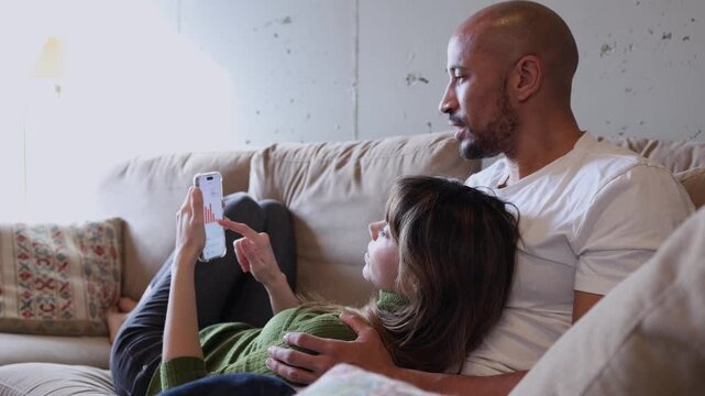 Relaxed couple analyzing financial charts on smartphone at home