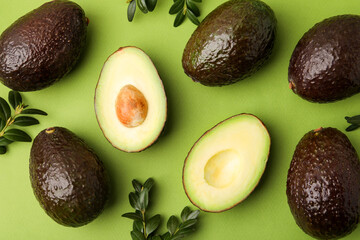 Fototapeta premium Fresh ripe avocados and leaves on green background, flat lay