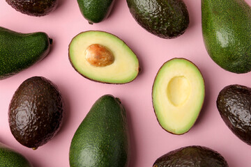 Fototapeta premium Whole and cut avocados on pink background, flat lay
