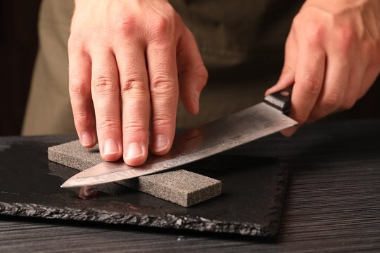 Man sharpening knife at wooden table, closeup