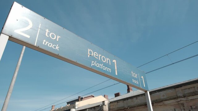 Blue directional sign at a railway station indicating platform one and track numbers against a clear sky