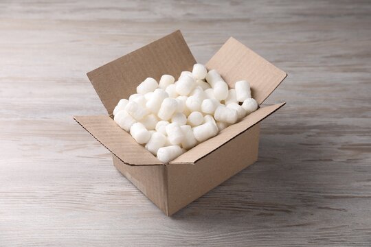 Cardboard box with styrofoam pieces on wooden background
