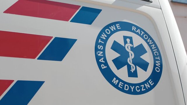 Close-up of a Polish emergency medical services logo and red reflective stripes on a white ambulance side