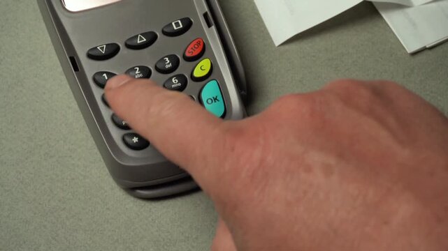 Hand inserting card and pressing buttons on payment terminal during a transaction at a retail checkout counter