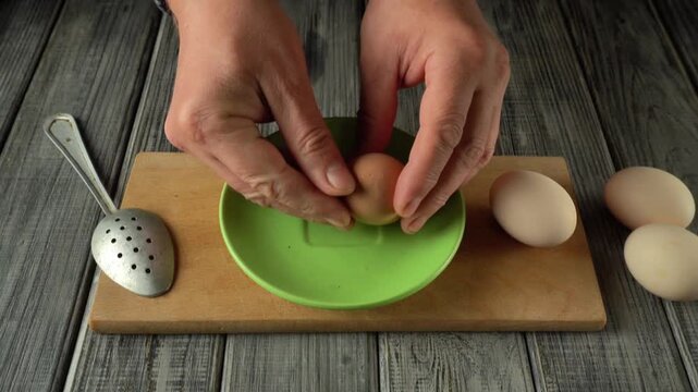 Hands cracking an egg into a green bowl using a slotted spoon on a wooden cutting board with additional eggs in the background